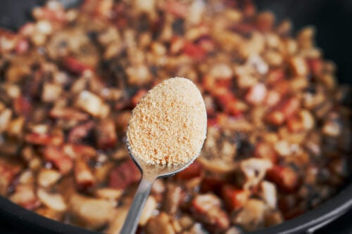 adding garlic powder seasoning to mushrooms and bacon
