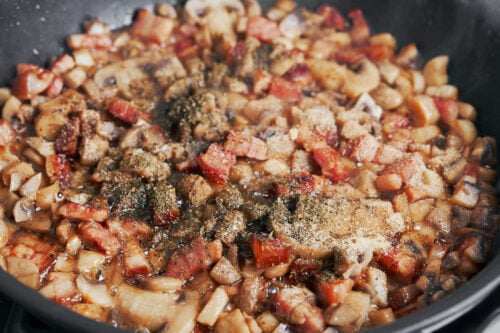 seasoned mushrooms and bacon cooking in a skillet