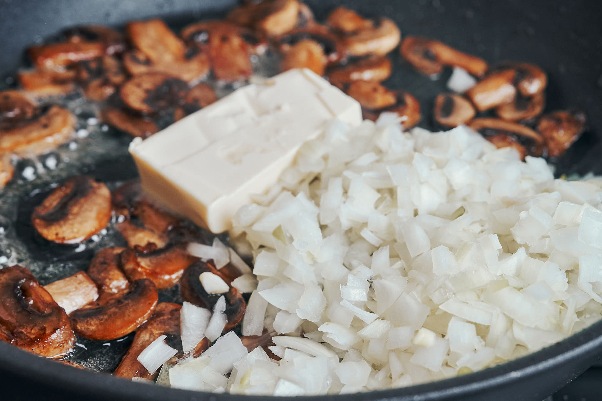 adding chopped onion and butter to mushrooms in a skillet