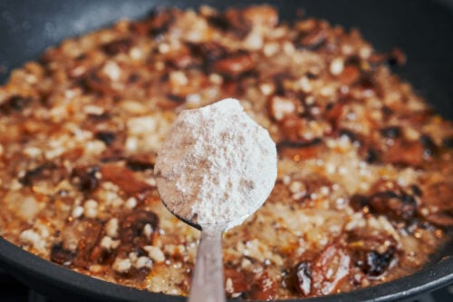 adding flour to mushrooms and onions in a skillet