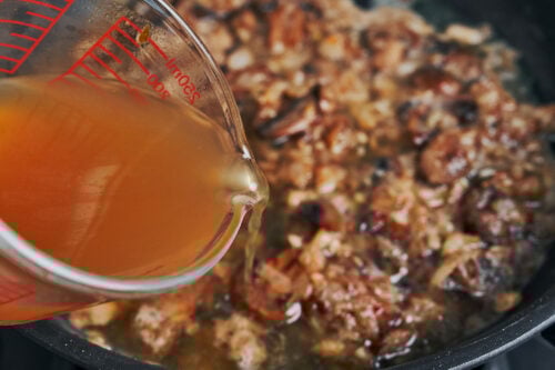 pouring broth into mushrooms and onions to build the sauce