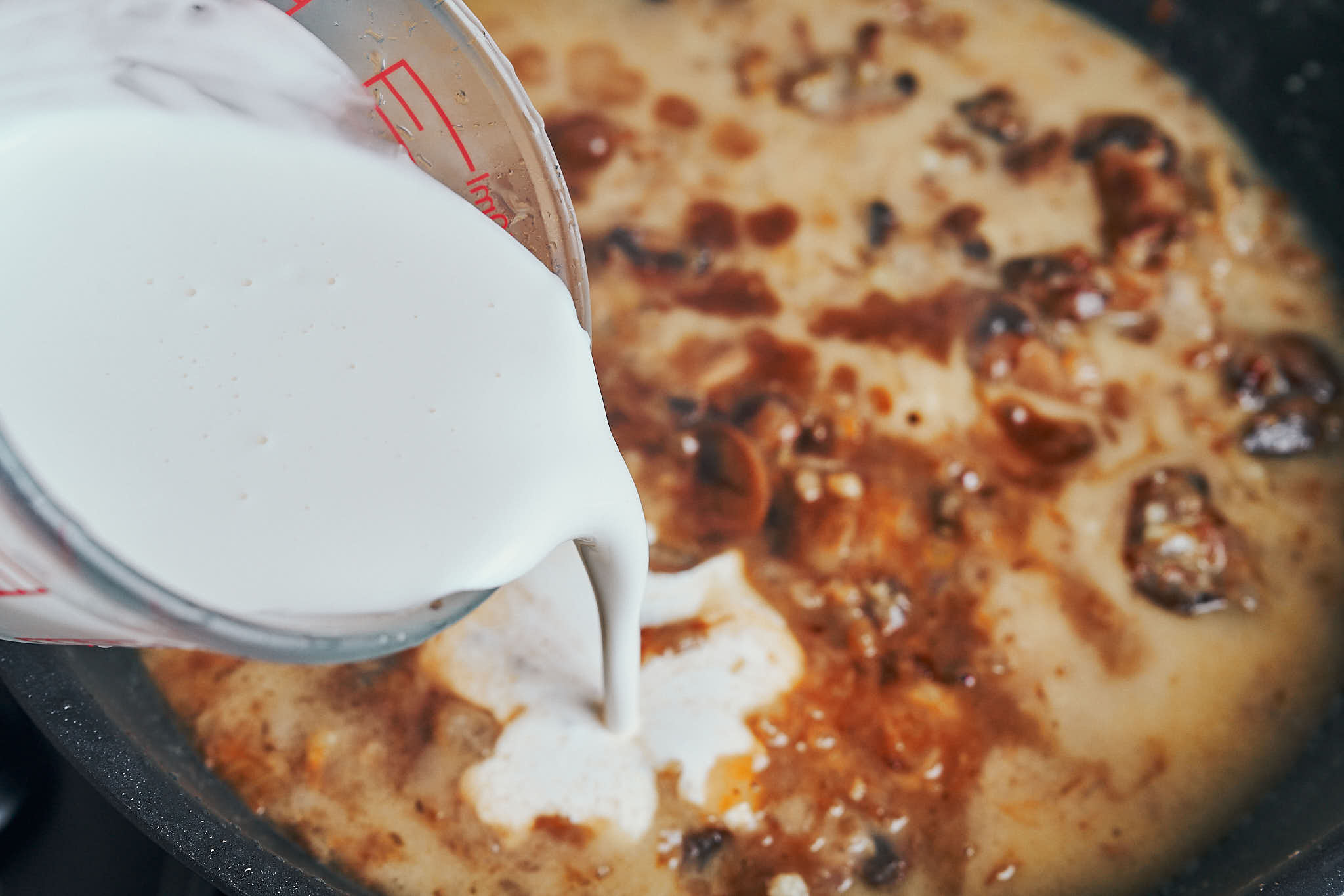 pouring heavy cream into mushroom sauce in a skillet