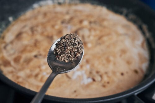 adding black pepper to creamy mushroom sauce