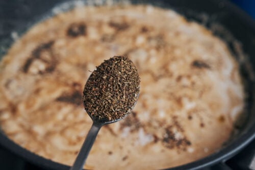 adding dried thyme to creamy mushroom sauce