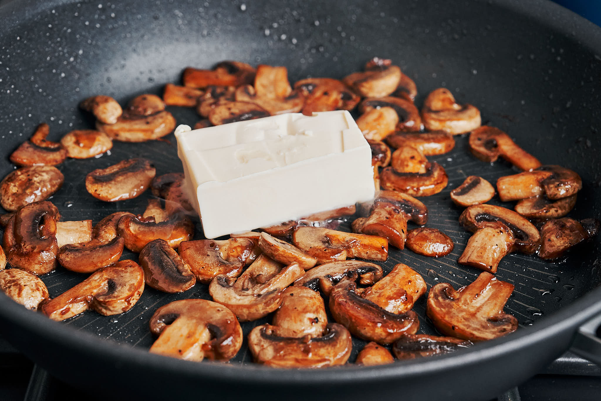 butter melting over browned mushrooms in a skillet