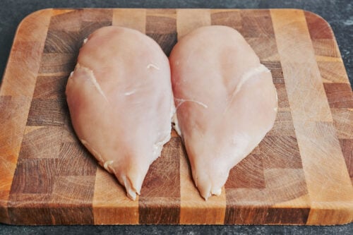 Raw chicken breasts on a wooden cutting board before slicing