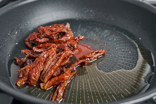 Sliced sun-dried tomatoes added to a skillet