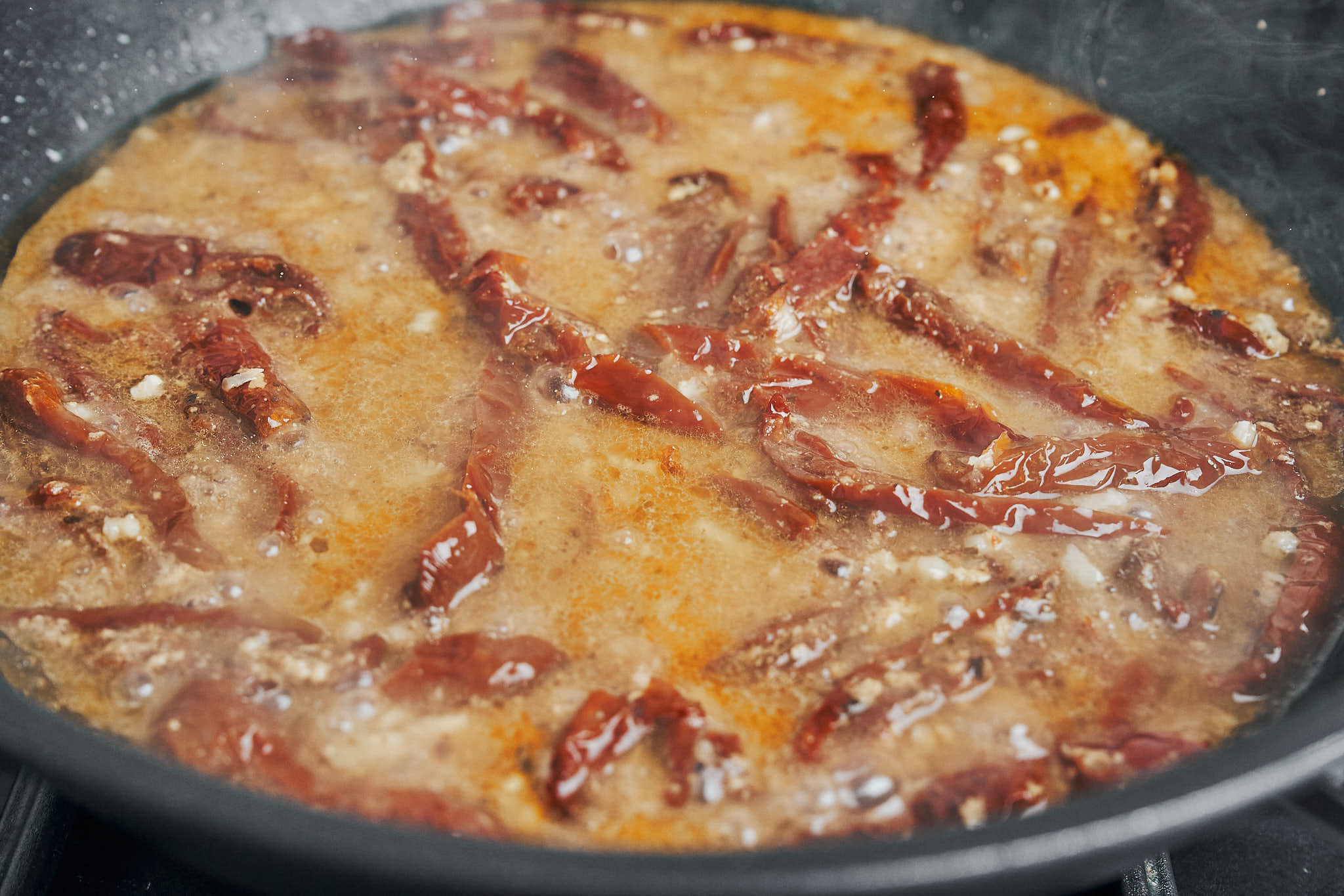 Creamy sauce simmering with sun-dried tomatoes in a skillet