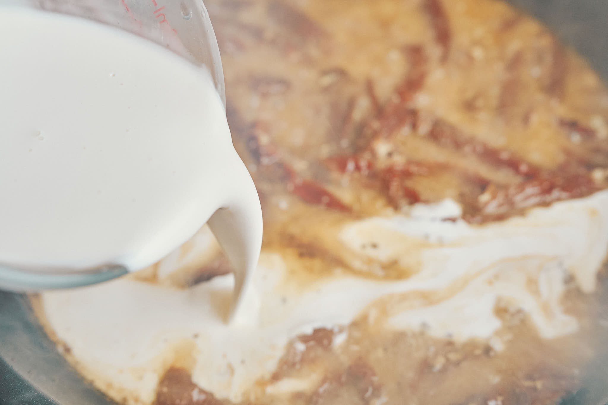 Heavy cream being poured into the skillet to make the sauce