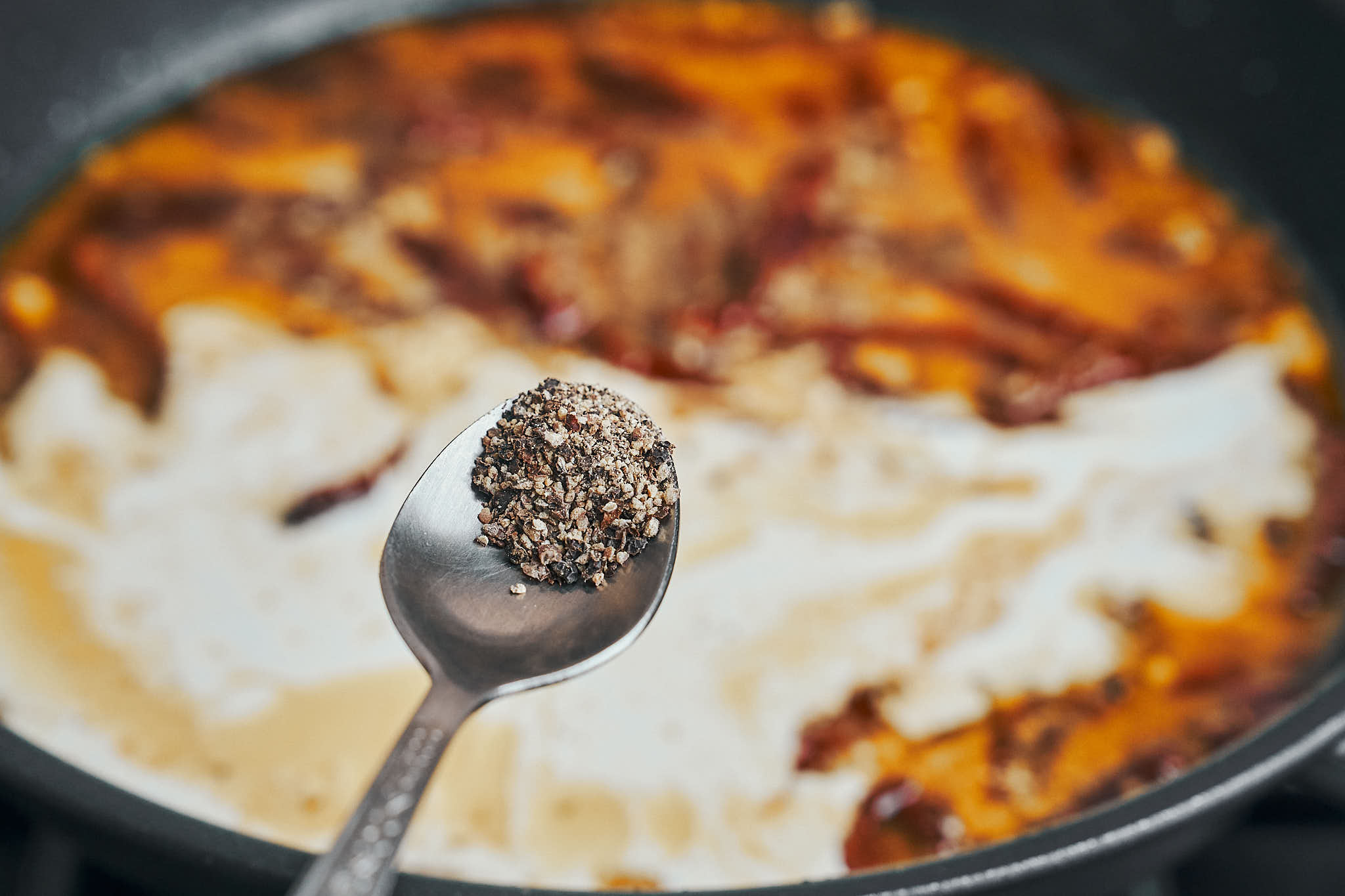 Black pepper added to the creamy sauce in a skillet