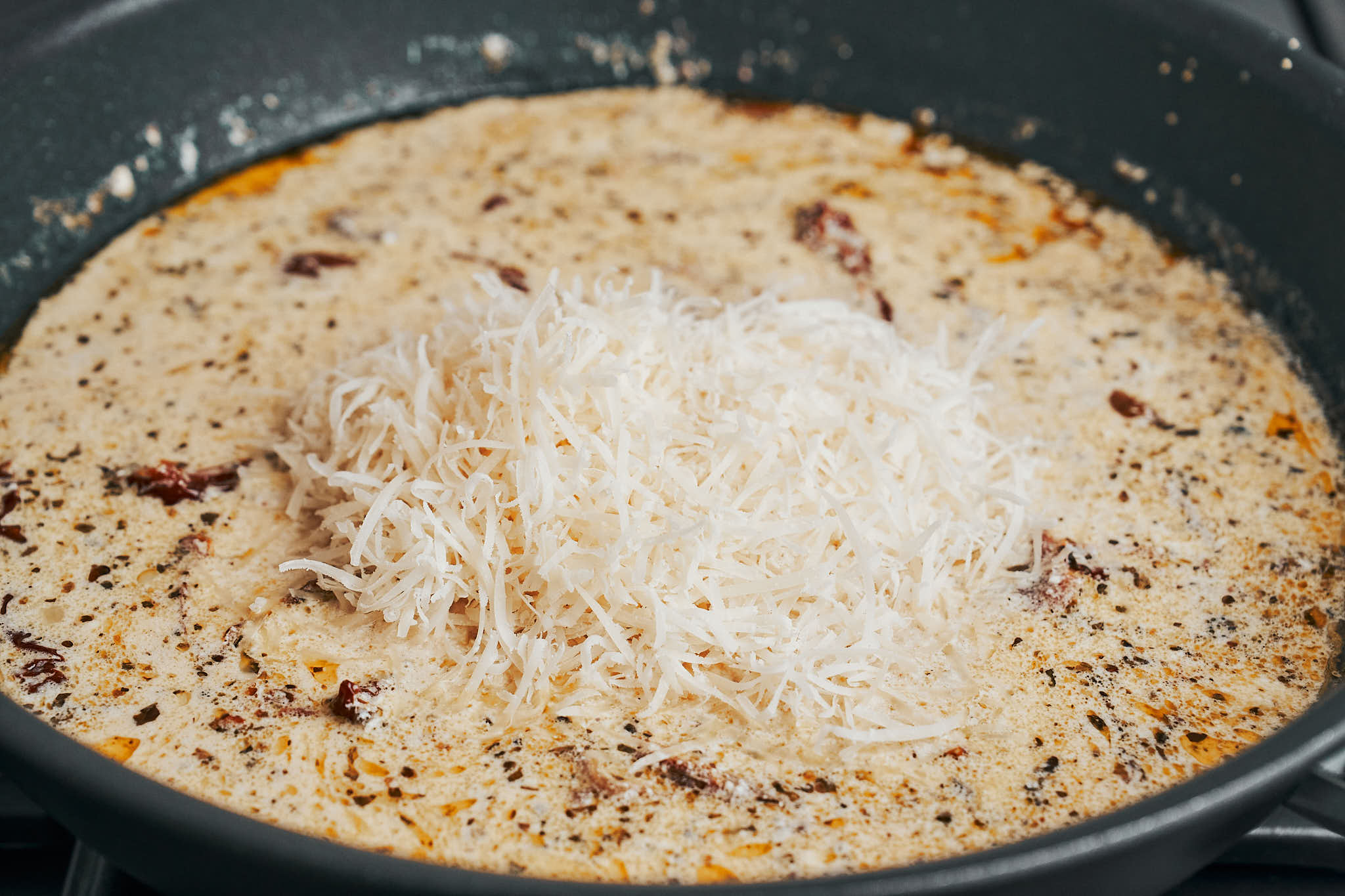 Grated parmesan cheese added to the creamy sauce in a skillet