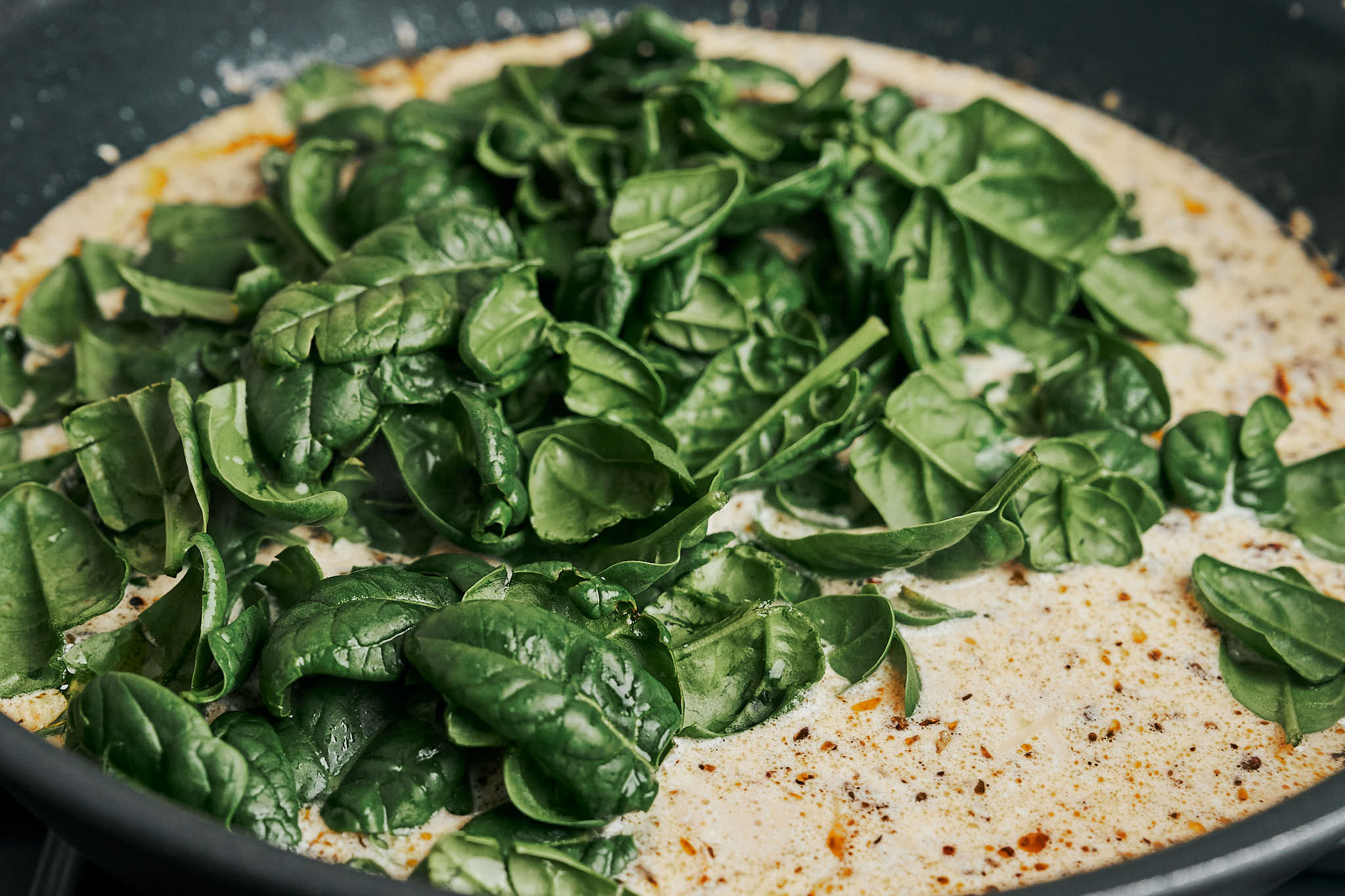 Fresh baby spinach added to the creamy sauce in a skillet