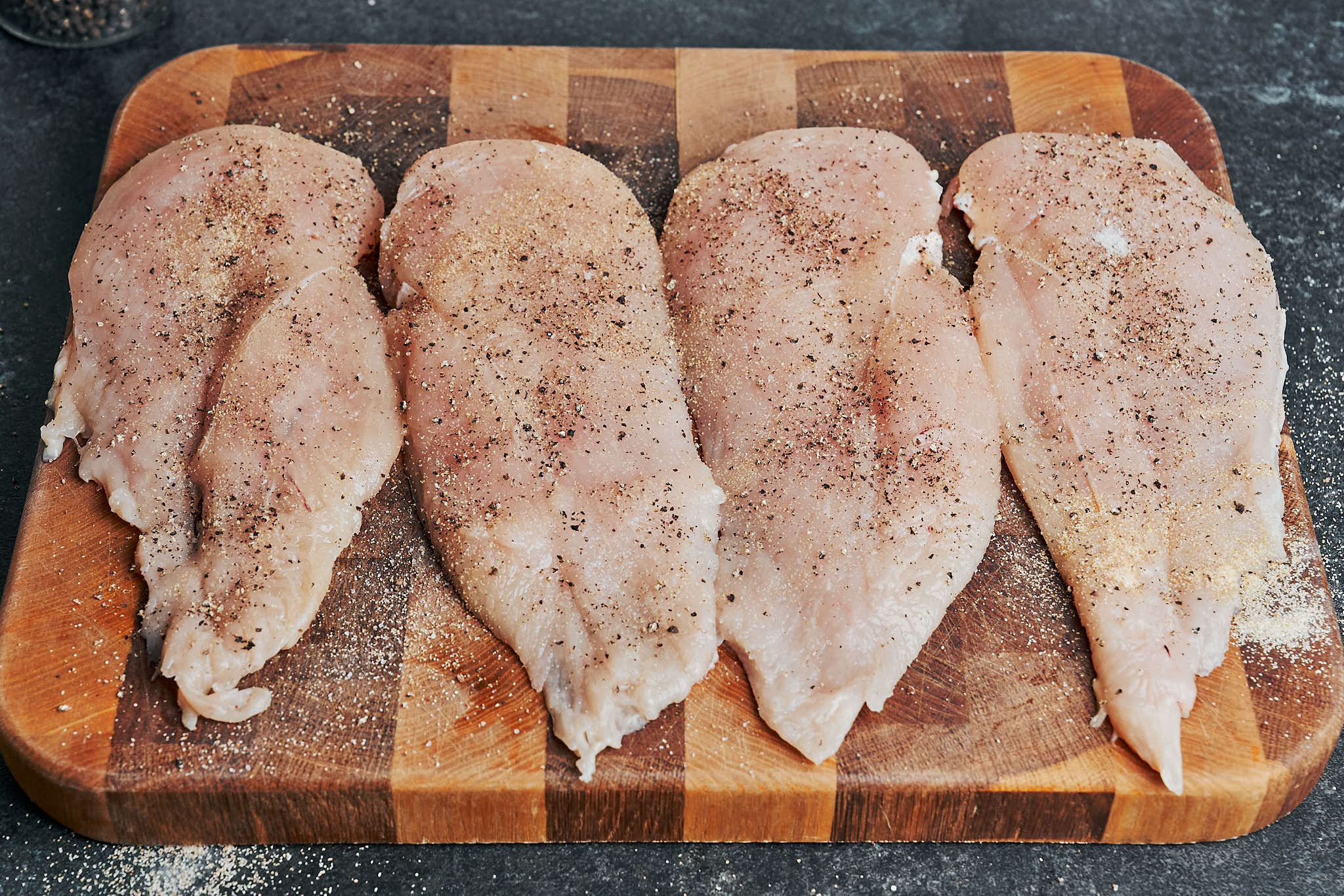 Seasoned chicken cutlets with salt, pepper, and garlic powder on a cutting board