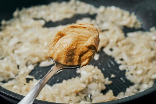 adding Dijon mustard to onions in a skillet