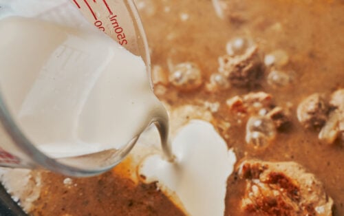 pouring heavy cream into the skillet to finish the sauce