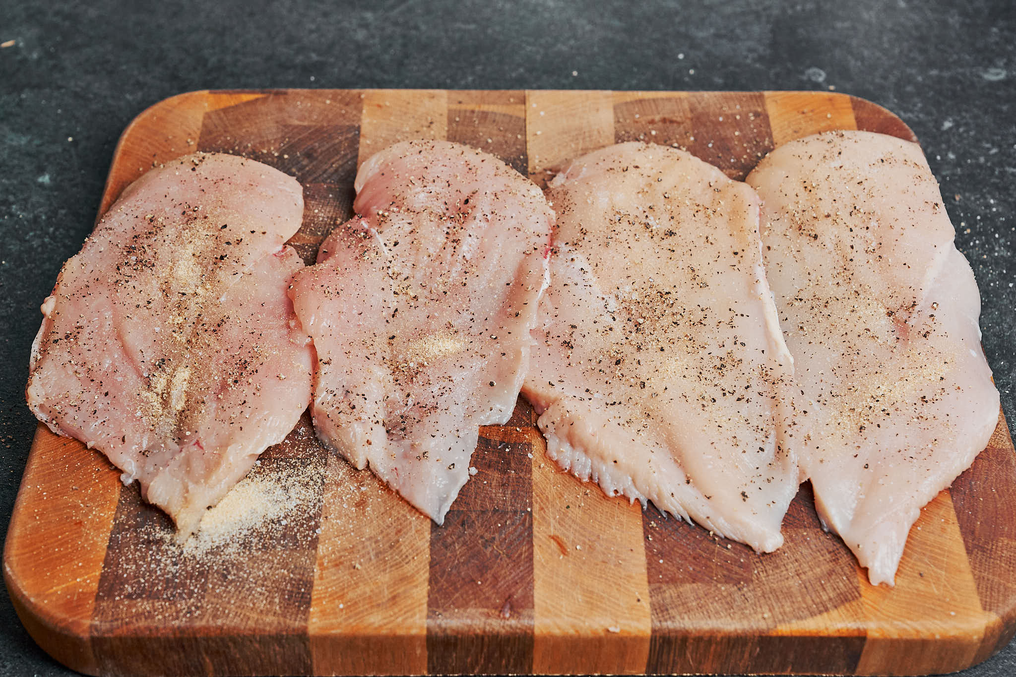 sliced chicken breasts seasoned with salt, pepper, and garlic powder on a wooden cutting board