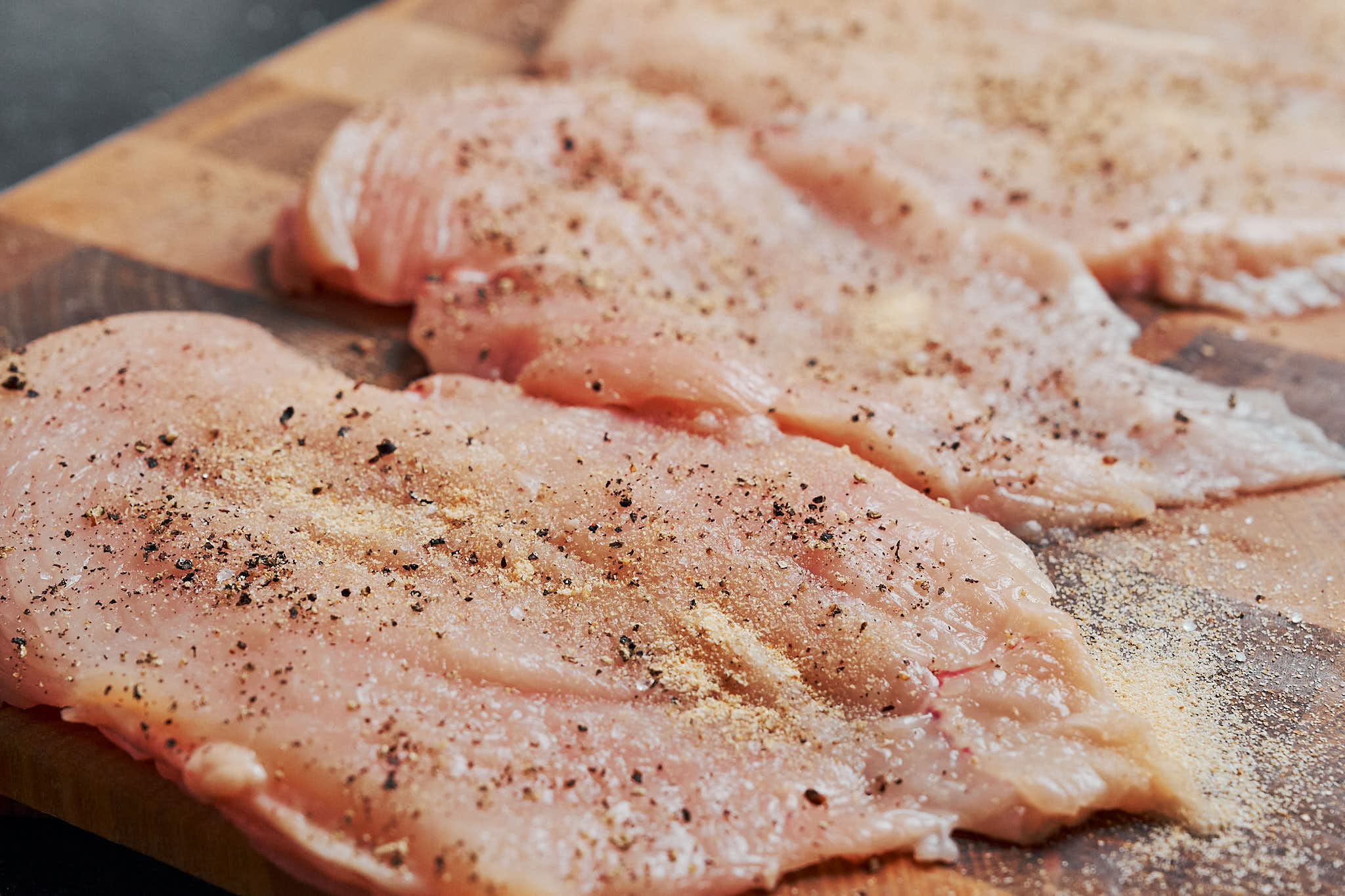 seasoned chicken breasts on a cutting board, ready to be cooked in a skillet