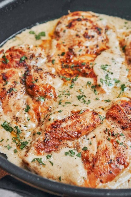 creamy parmesan chicken simmering in a skillet with fresh parsley