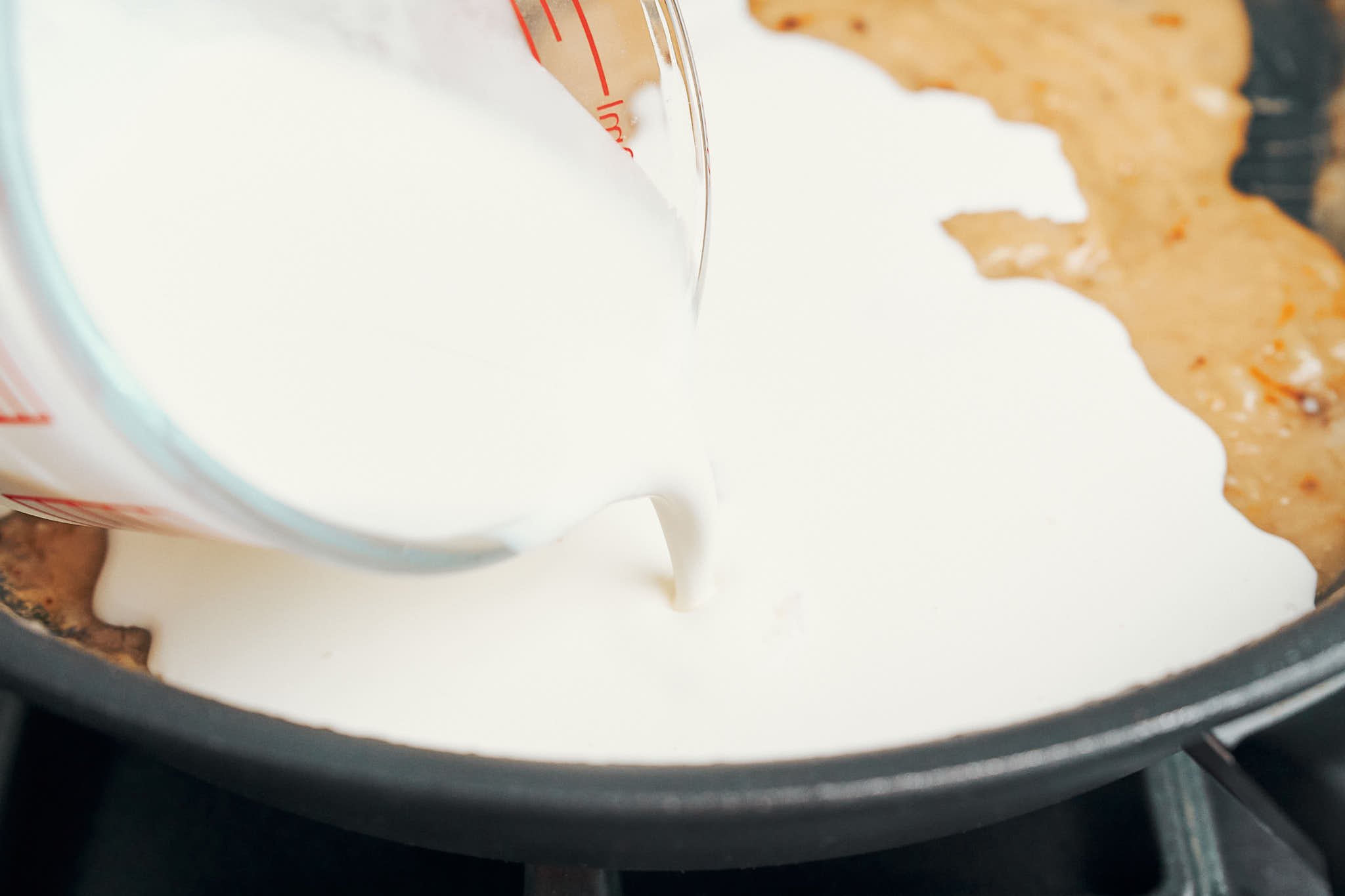 pouring heavy cream into the skillet as the sauce turns smooth and creamy