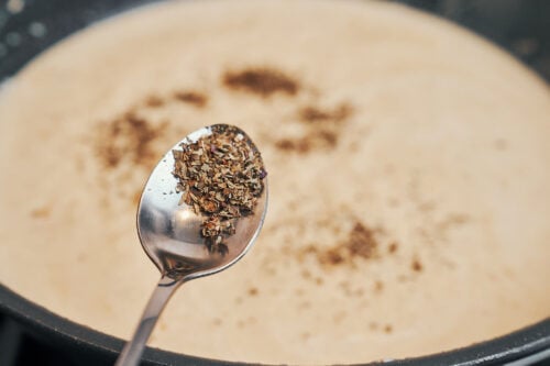 sprinkling basil into the sauce as it simmers