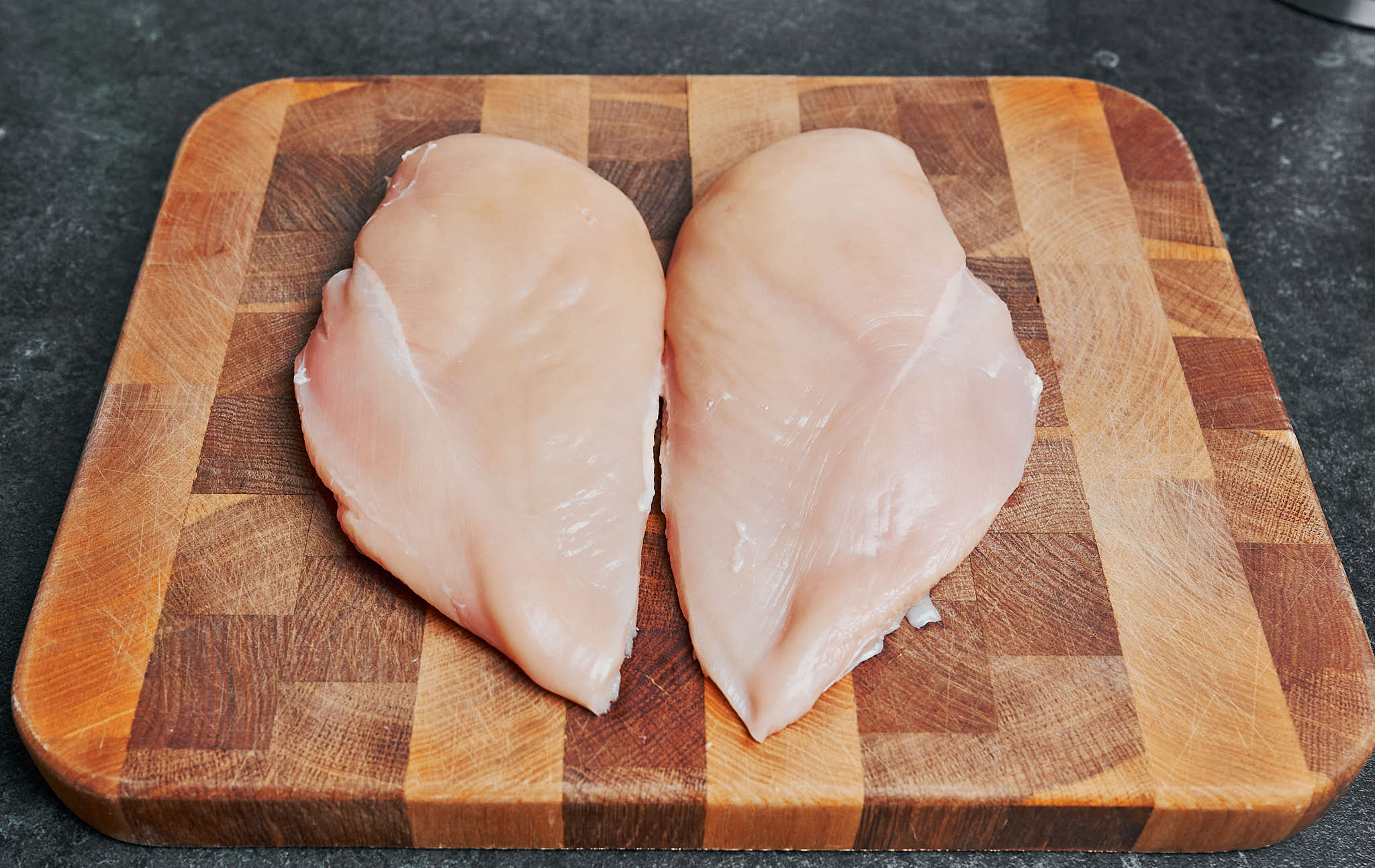 raw chicken breasts on a wooden cutting board, ready to be prepped for creamy parmesan chicken