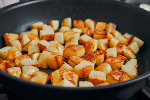 potatoes starting to turn golden as they cook in the skillet
