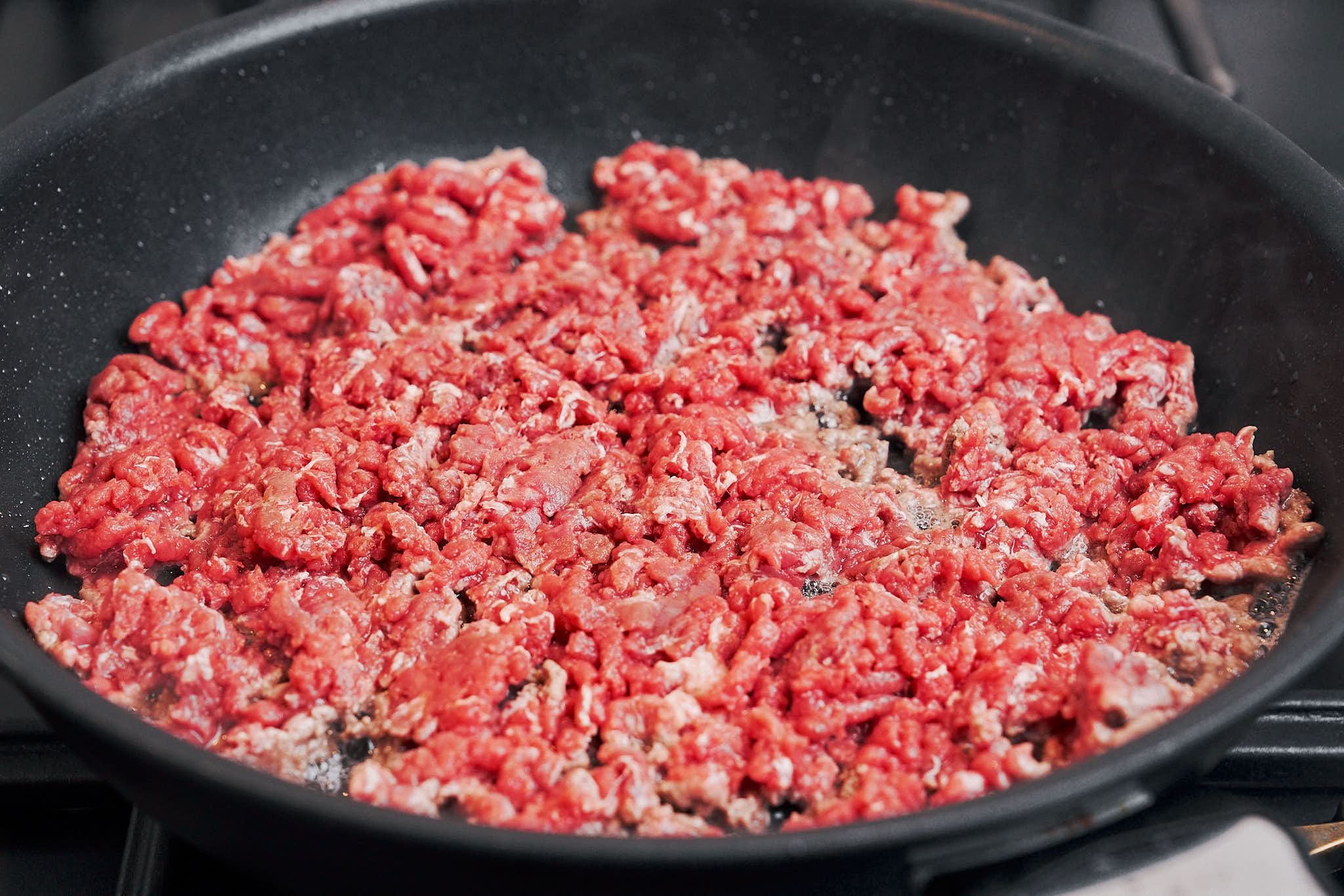 ground beef cooking in the skillet as it starts to brown and release flavor