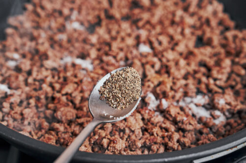 sprinkling black pepper over browned ground beef