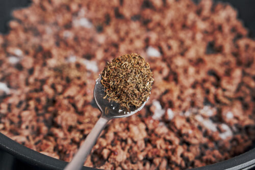 adding dried thyme to browned ground beef in the skillet