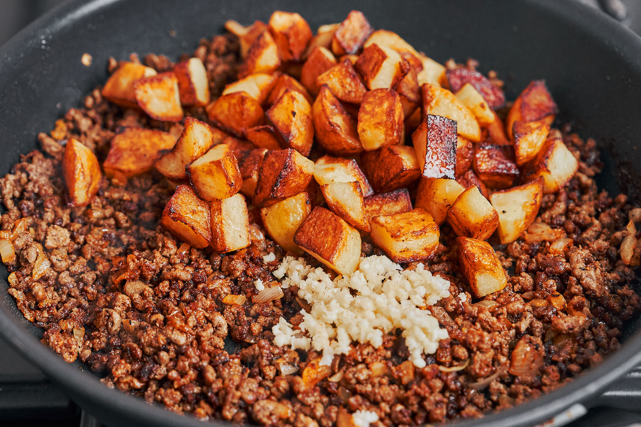 adding crispy potatoes back into the skillet with ground beef and garlic