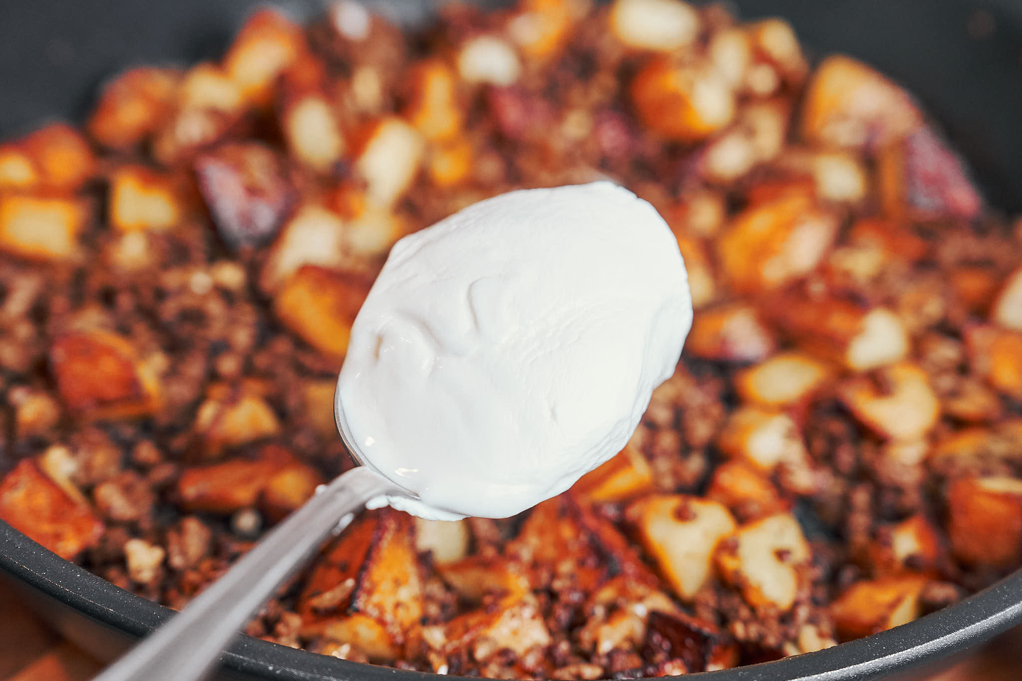 spoonful of sour cream about to be mixed into the ground beef and potatoes