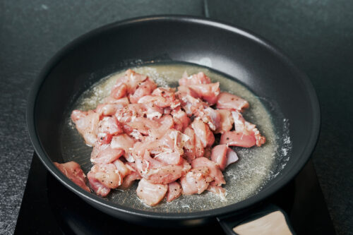 diced chicken thighs added to a skillet for searing