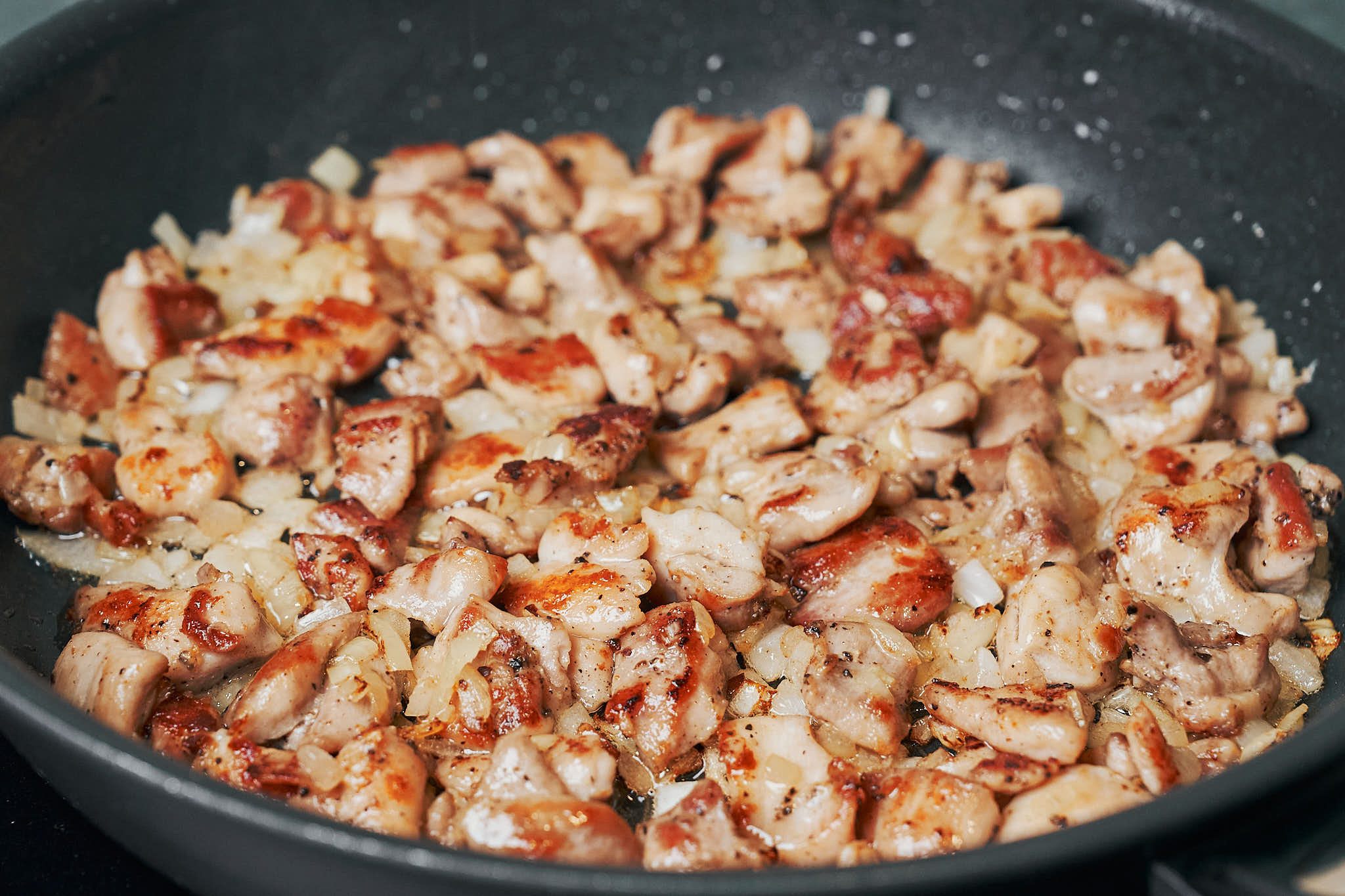 chicken thighs cooking with diced onion in a skillet