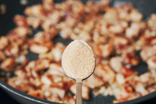 adding garlic powder to chicken cooking in a skillet