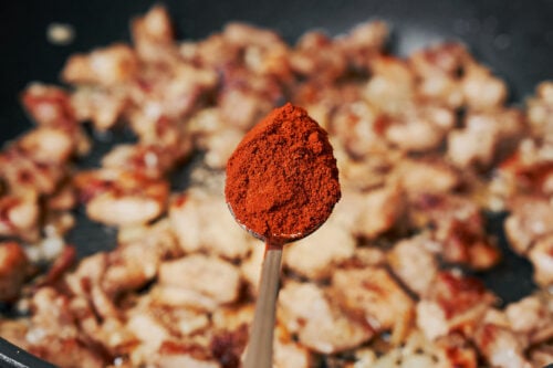 adding paprika to chicken and onion in a skillet