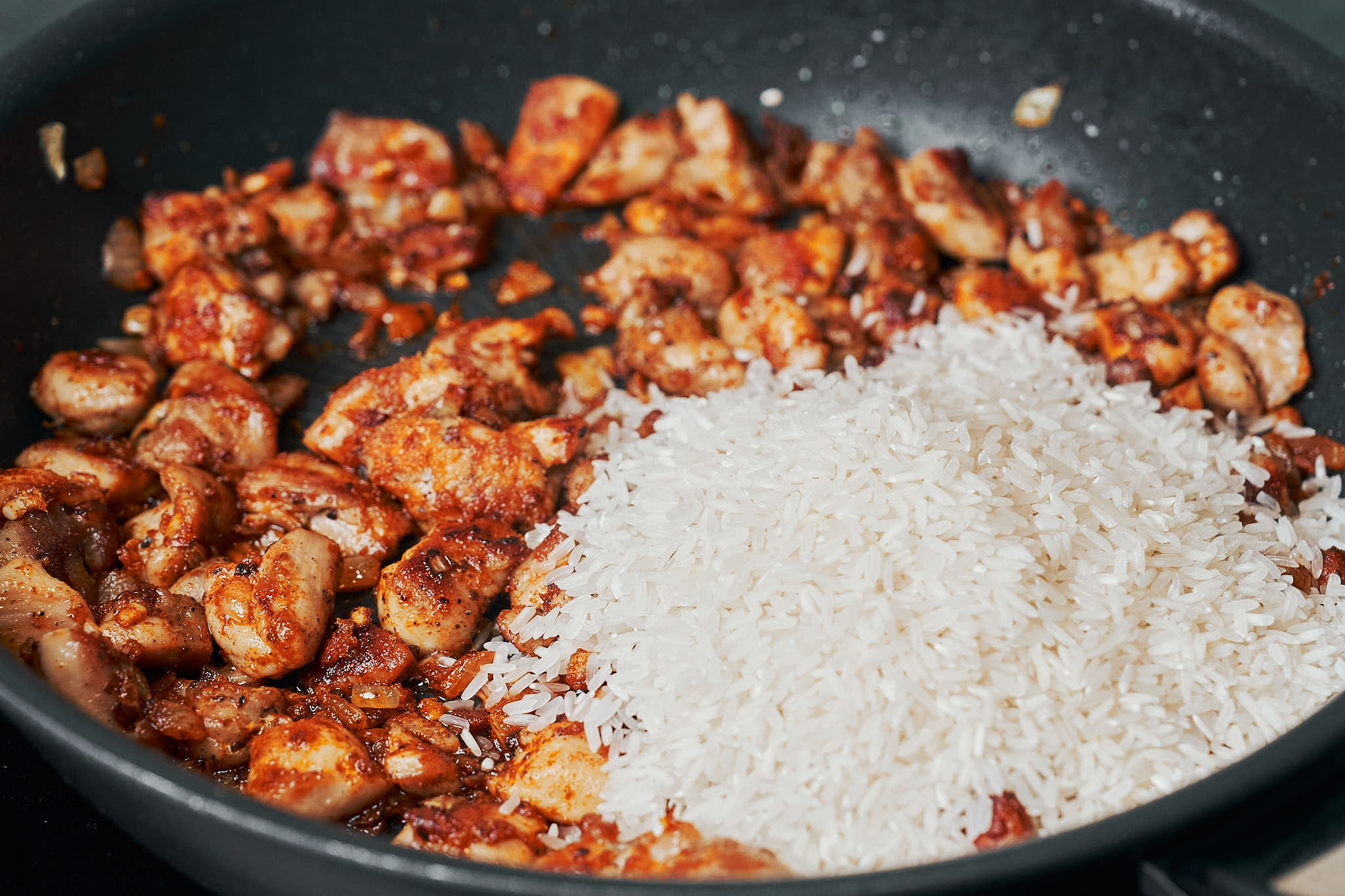 long grain white rice added to chicken in a skillet
