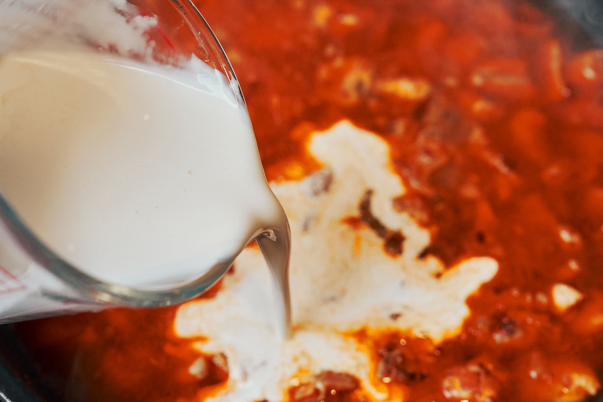 heavy cream being poured into chicken and rice skillet