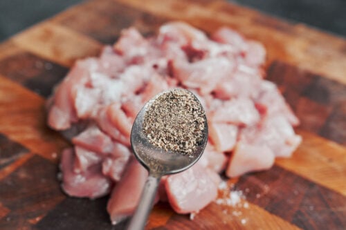 adding black pepper to diced chicken thighs before cooking