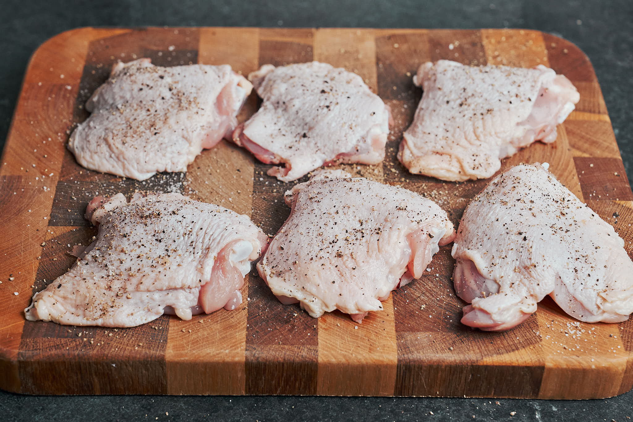 raw chicken thighs seasoned with salt and black pepper on wooden cutting board
