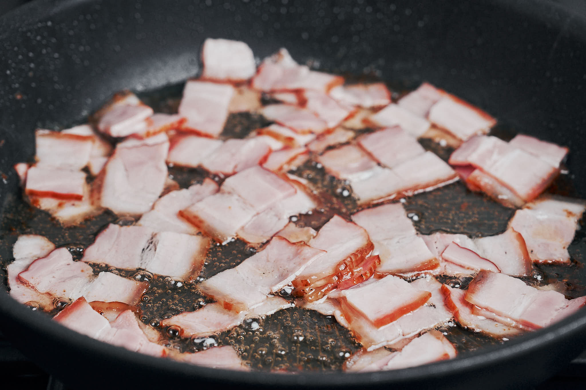 chopped bacon cooking in skillet to render fat