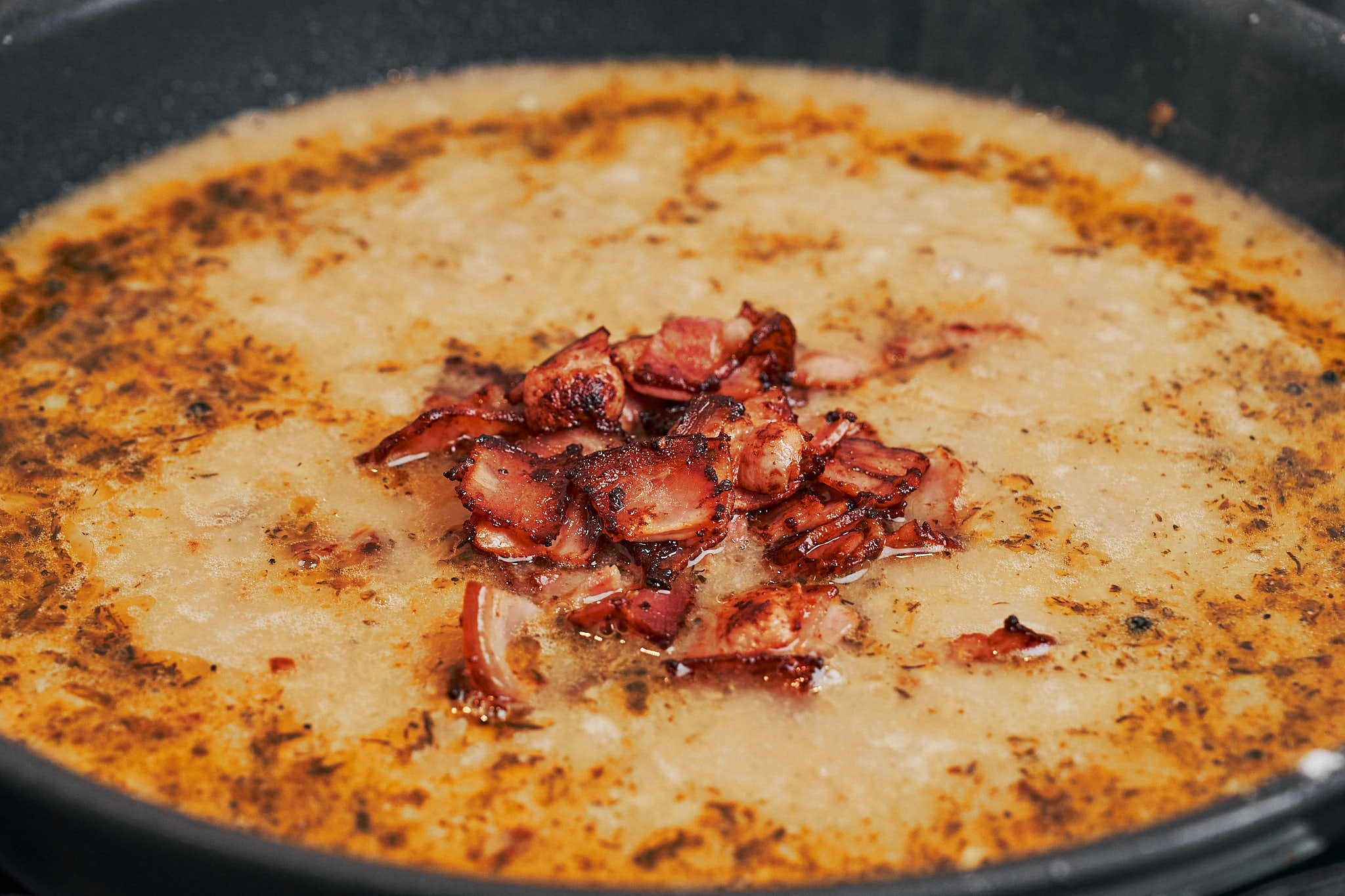 crispy bacon added to creamy sauce in skillet