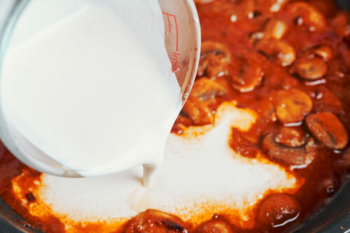 pouring heavy cream into skillet to make the sauce creamy