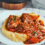Hearty pork stew with red bell peppers and fresh parsley served over creamy mashed potatoes