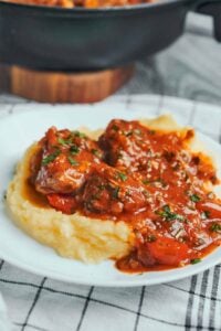 Hearty pork stew with red bell peppers and fresh parsley served over creamy mashed potatoes