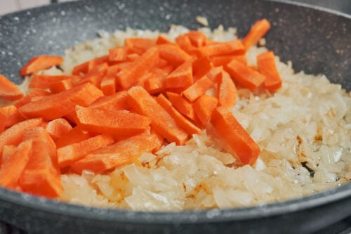 adding sliced carrots to sautéed onions in skillet