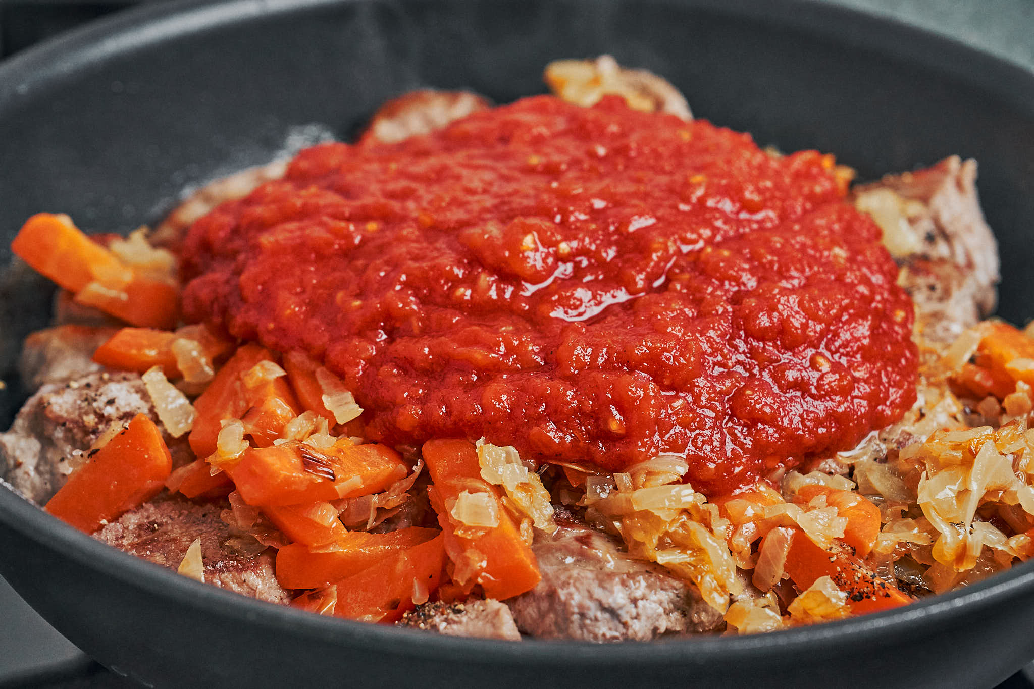tomato mixture poured over pork and vegetables in skillet