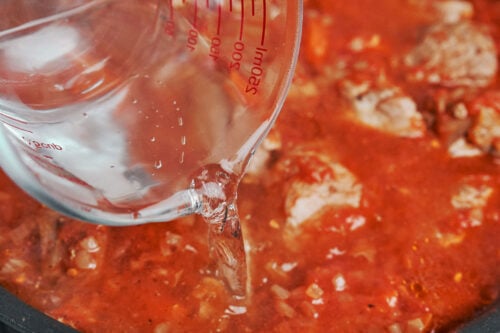 pouring water into pork stew before simmering