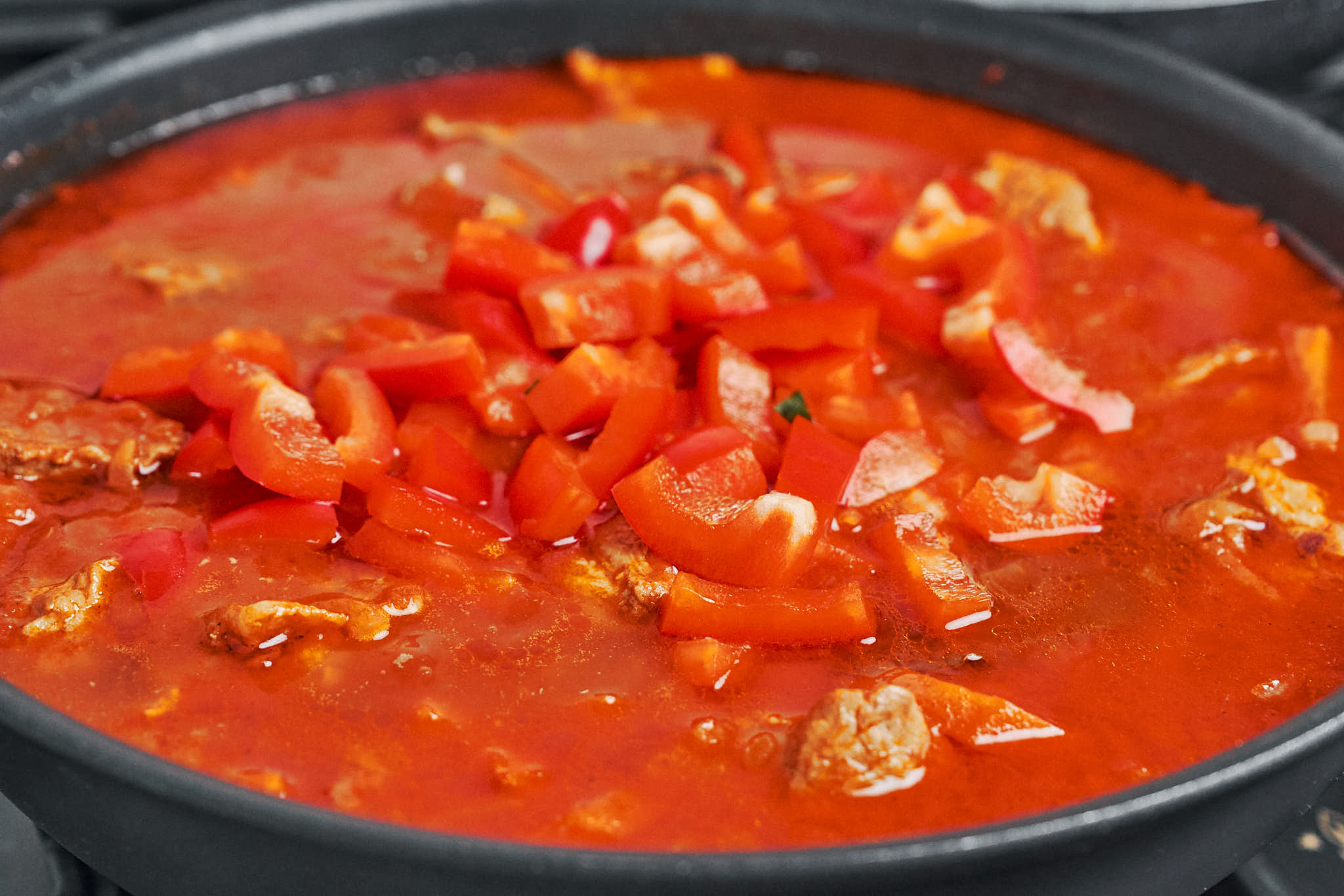 adding chopped red bell pepper to simmering pork stew