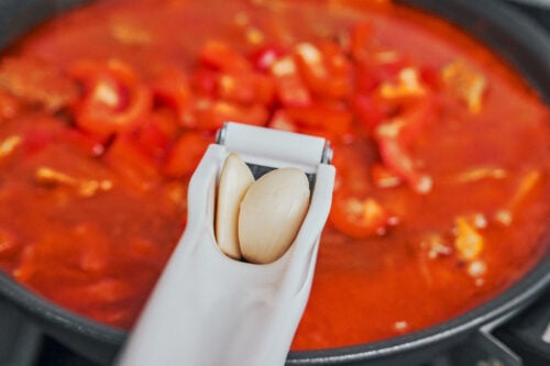 pressing fresh garlic into simmering pork stew