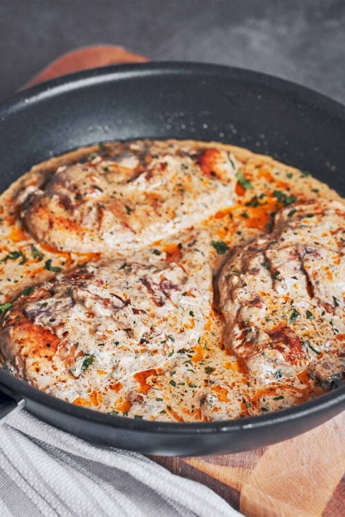 creamy sun dried tomato chicken in a skillet with fresh parsley